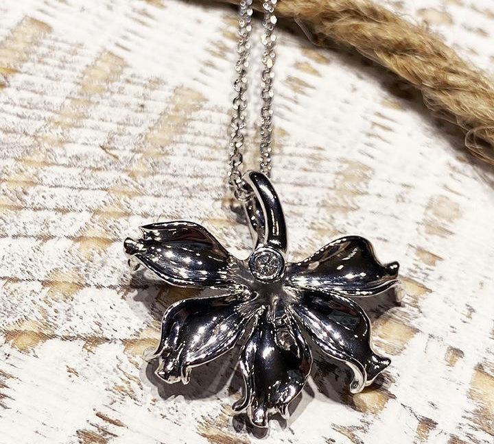 In this photo there is a white gold naupaka flower pendant with one diamond.