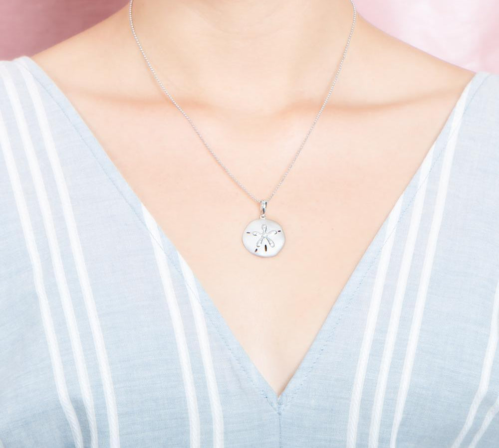 The picture shows a model wearing a white gold sand dollar pendant with topaz.