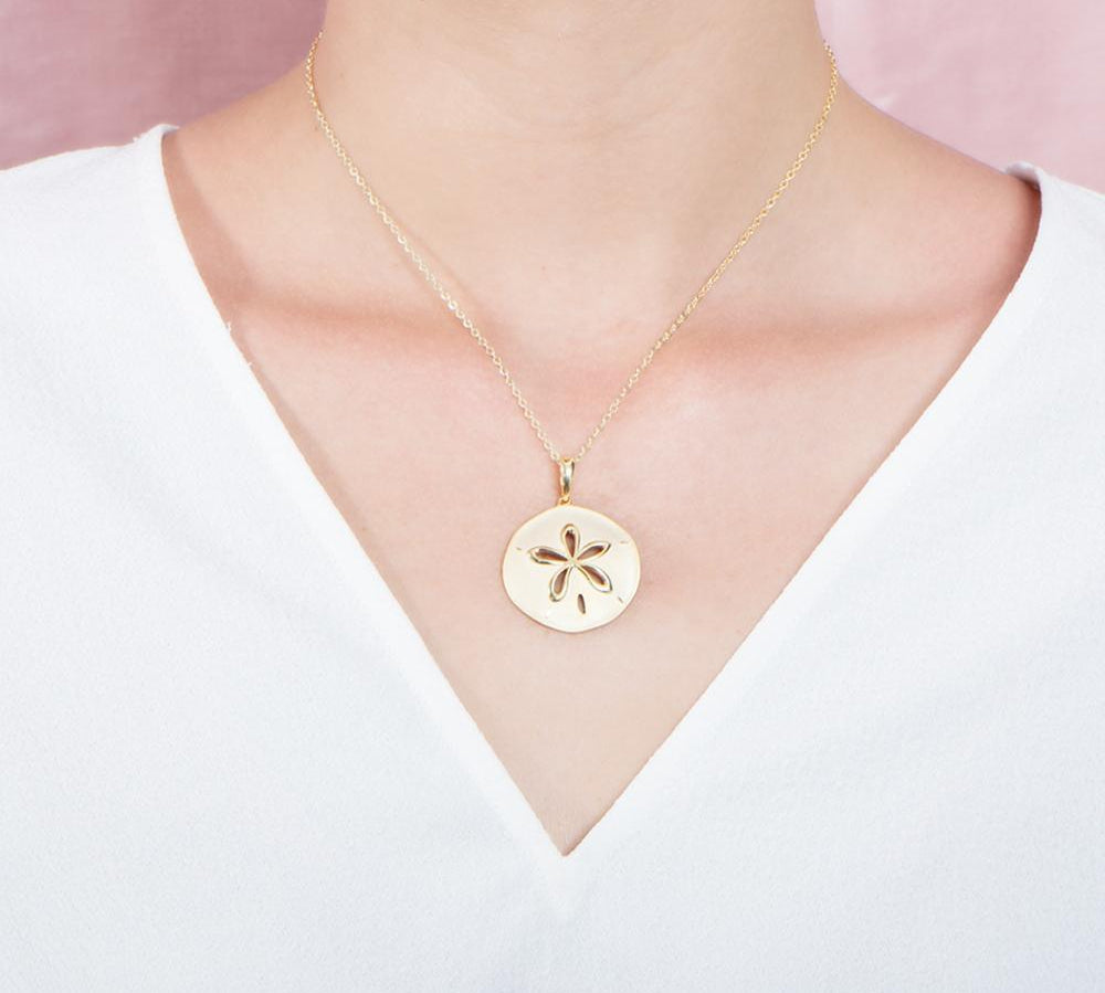 The picture shows a model wearing a 925 sterling silver, yellow gold plated, sand dollar cut out pendant with topaz.