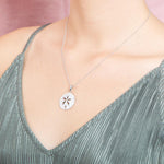 The picture shows a model wearing a 925 sterling silver, white gold plated, sand dollar cut out pendant with topaz.