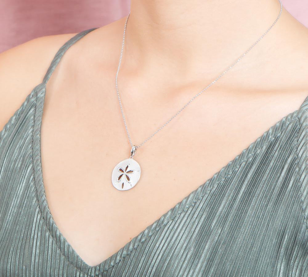 The picture shows a model wearing a 925 sterling silver, white gold plated, sand dollar cut out pendant with topaz.