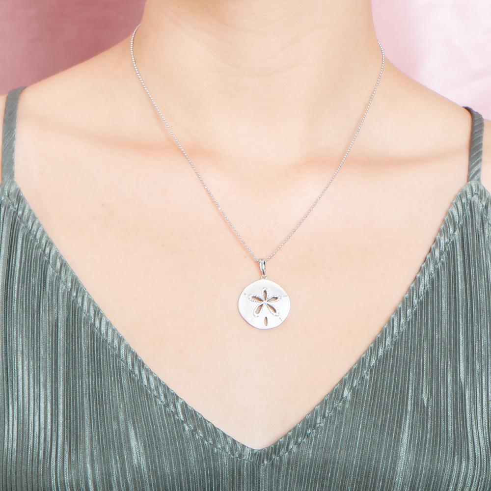 The picture shows a model wearing a 925 sterling silver, white gold plated, sand dollar cut out pendant with topaz.