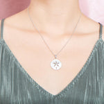 The picture shows a model wearing a 925 sterling silver, white gold plated, sand dollar cut out pendant with topaz.