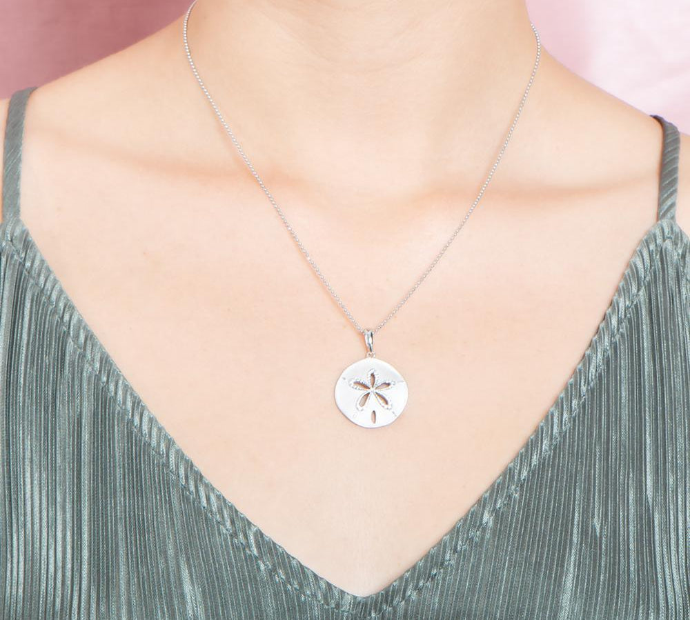 The picture shows a model wearing a 925 sterling silver, white gold plated, sand dollar cut out pendant with topaz.