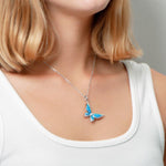 In this photo there is a model turned to the right with strawberry blonde hair and a white shirt, wearing a sterling silver butterfly pendant with blue opalite gemstones and topaz.