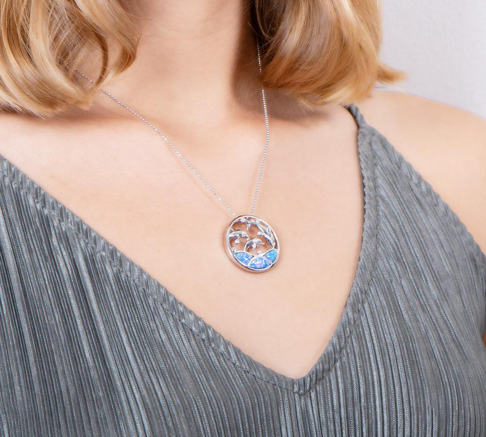 The picture shows a model wearing a 925 sterling silver opalite three jumping dolphins pendant with topaz.