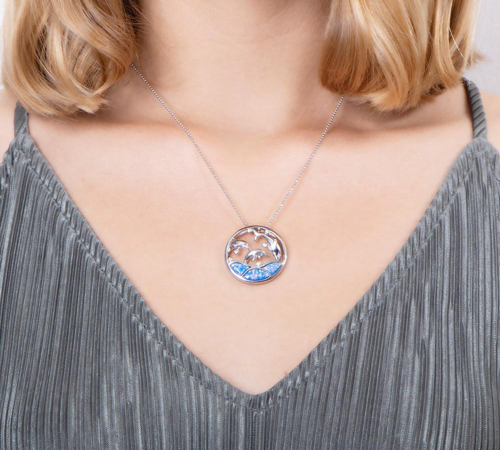The picture shows a model wearing a 925 sterling silver opalite three jumping dolphins pendant with topaz.