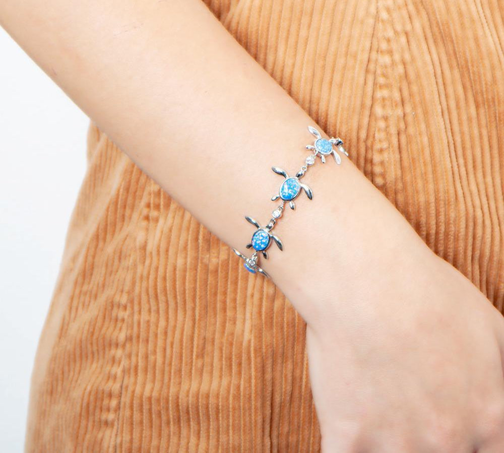 The picture shows a model wearing a 925 sterling silver opalite sea turtle charm bracelet with cubic zirconia.
