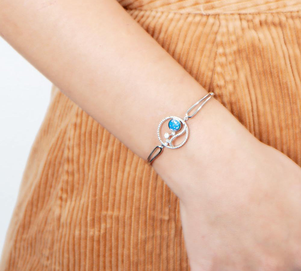 In this photo there is a model wearing a sterling silver wave and sun bracelet with blue opalite, aquamarine and topaz gemstones