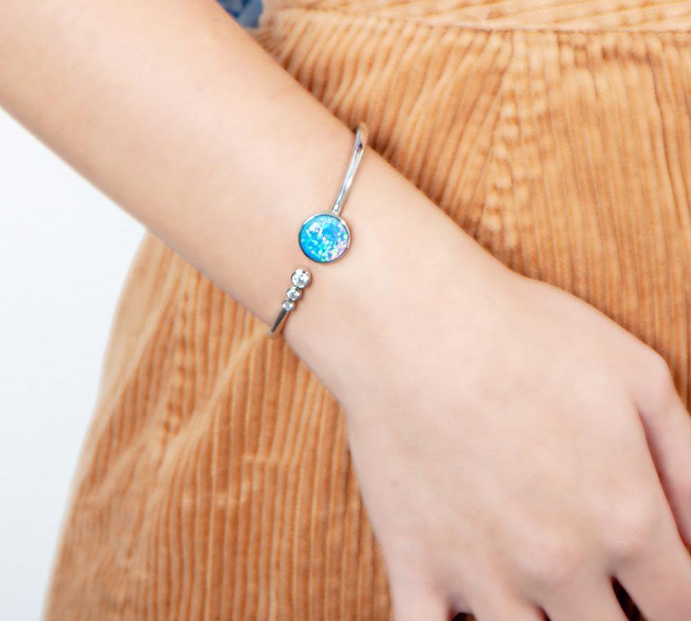 The picture shows a model wearing a 925 sterling silver opalite lunar orbit bangle with three topaz gemstones.