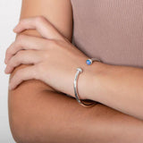 The picture shows a model wearing a 925 sterling silver bangle with two opalite gemstones and topaz.