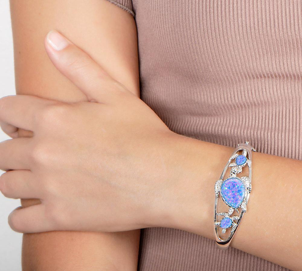 The picture shows a model wearing a 925 sterling silver family of three sea turtles bangle with opalite.
