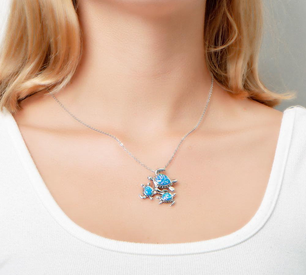The picture shows a model wearing a 925 sterling silver opalite family of three sea turtles pendant with topaz.