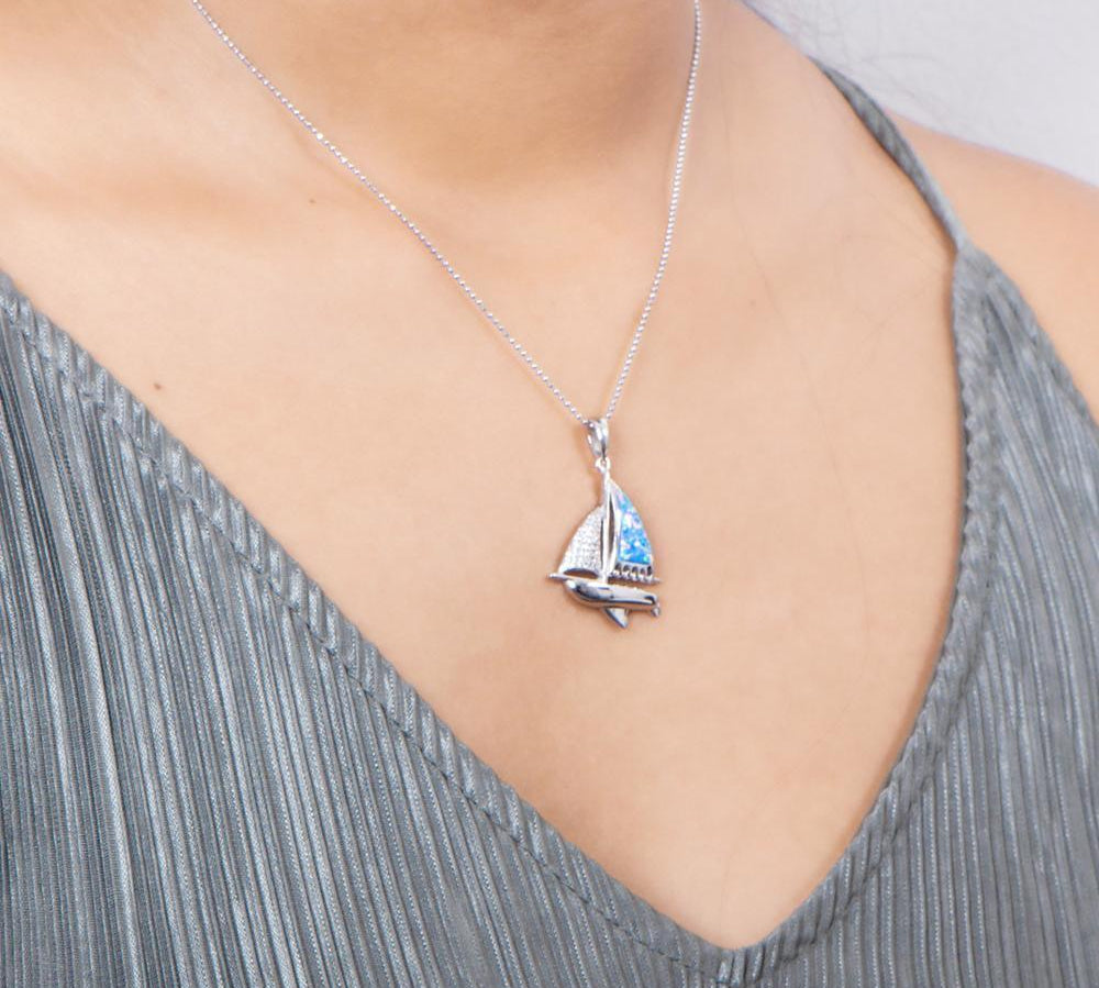 In this photo there is a model with a gray shirt turned slightly to the right, wearing a sterling silver sailboat pendant with blue opalite and topaz gemstones.