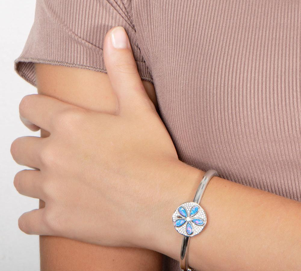 The picture shows a model wearing a 925 sterling silver sand dollar bangle with blue opalite and topaz.