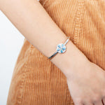 The picture shows a model wearing a 925 sterling silver sand dollar bangle with blue opalite and topaz.
