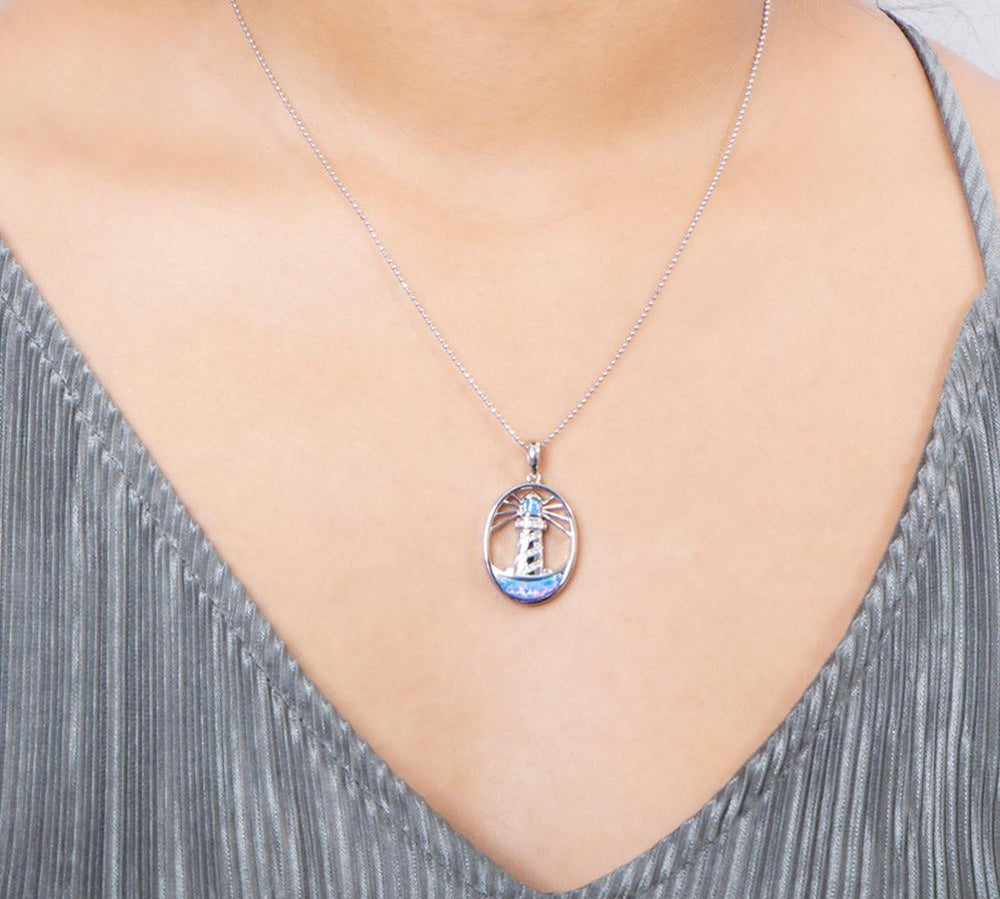 In this photo there is a model with a gray shirt wearing a sterling silver shining lighthouse pendant with blue opalite and topaz gemstones.