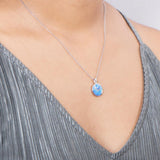 In this photo there is a model with a gray shirt turned slightly to the right, wearing a sterling silver circle pendant with blue opalite and topaz gemstones.