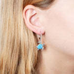 The picture shows a model wearing a 925 sterling silver opalite swimming sea turtle earring with cubic zirconia.