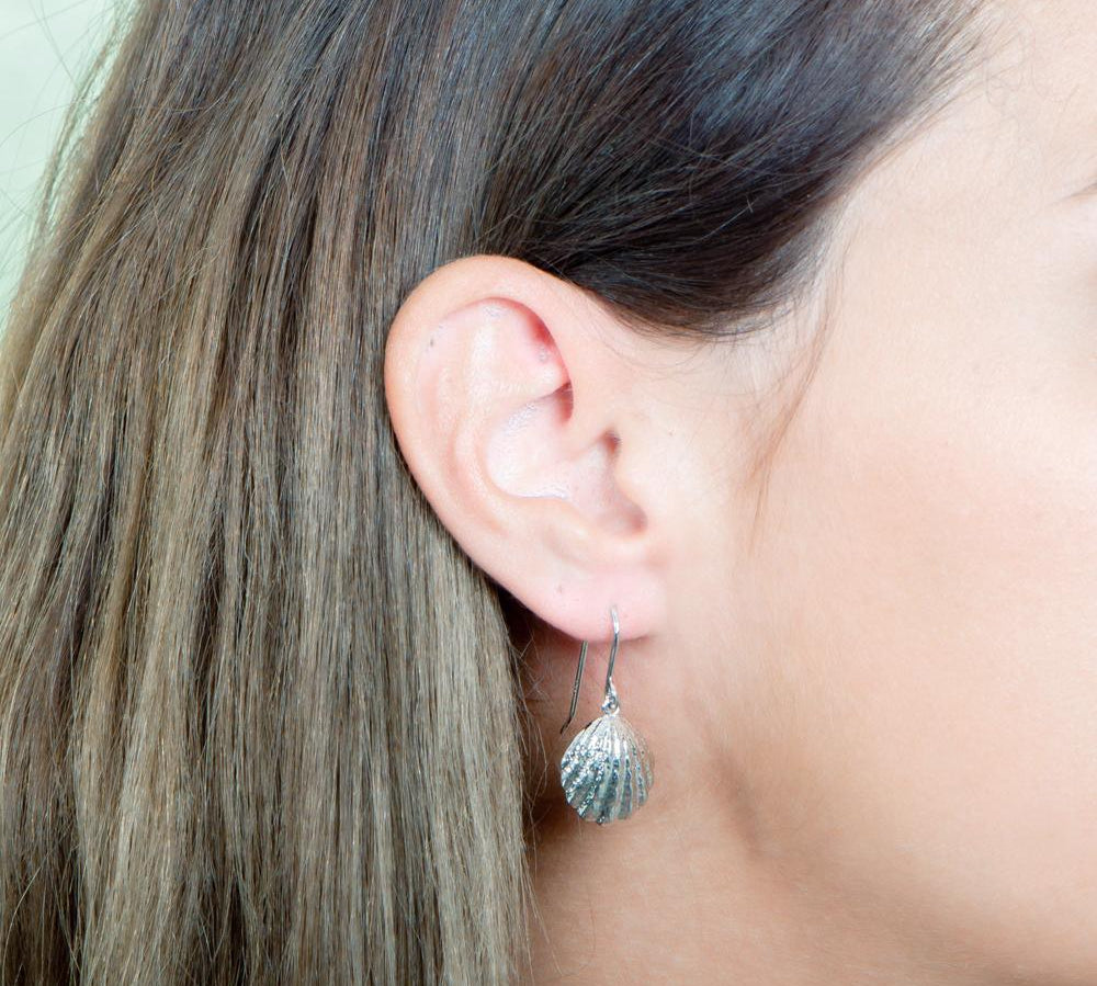 In this picture there is a close-up of a model in profile with brown hair wearing sterling silver oyster shell dangle earrings.