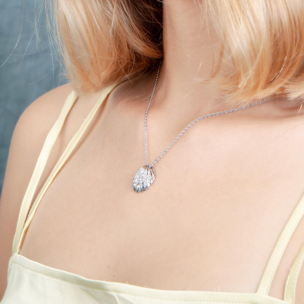 In this picture there is a model with blond hair and light yellow shirt turned to the left wearing a sterling silver oyster shell pendant.