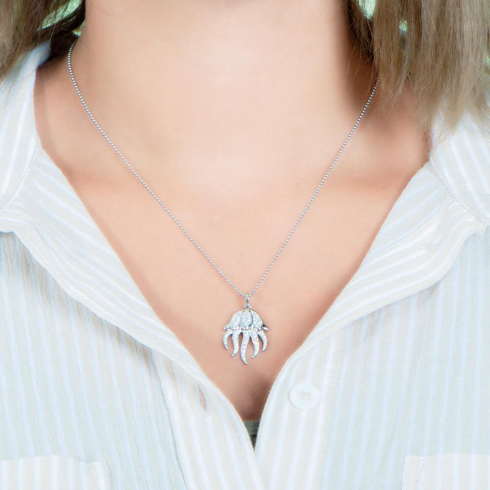 The picture shows a model wearing a 925 sterling silver, white gold plated, pavé barrel jellyfish pendant with topaz.
