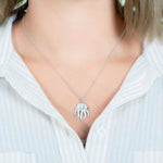 The picture shows a model wearing a 925 sterling silver, white gold plated, pavé barrel jellyfish pendant with topaz.