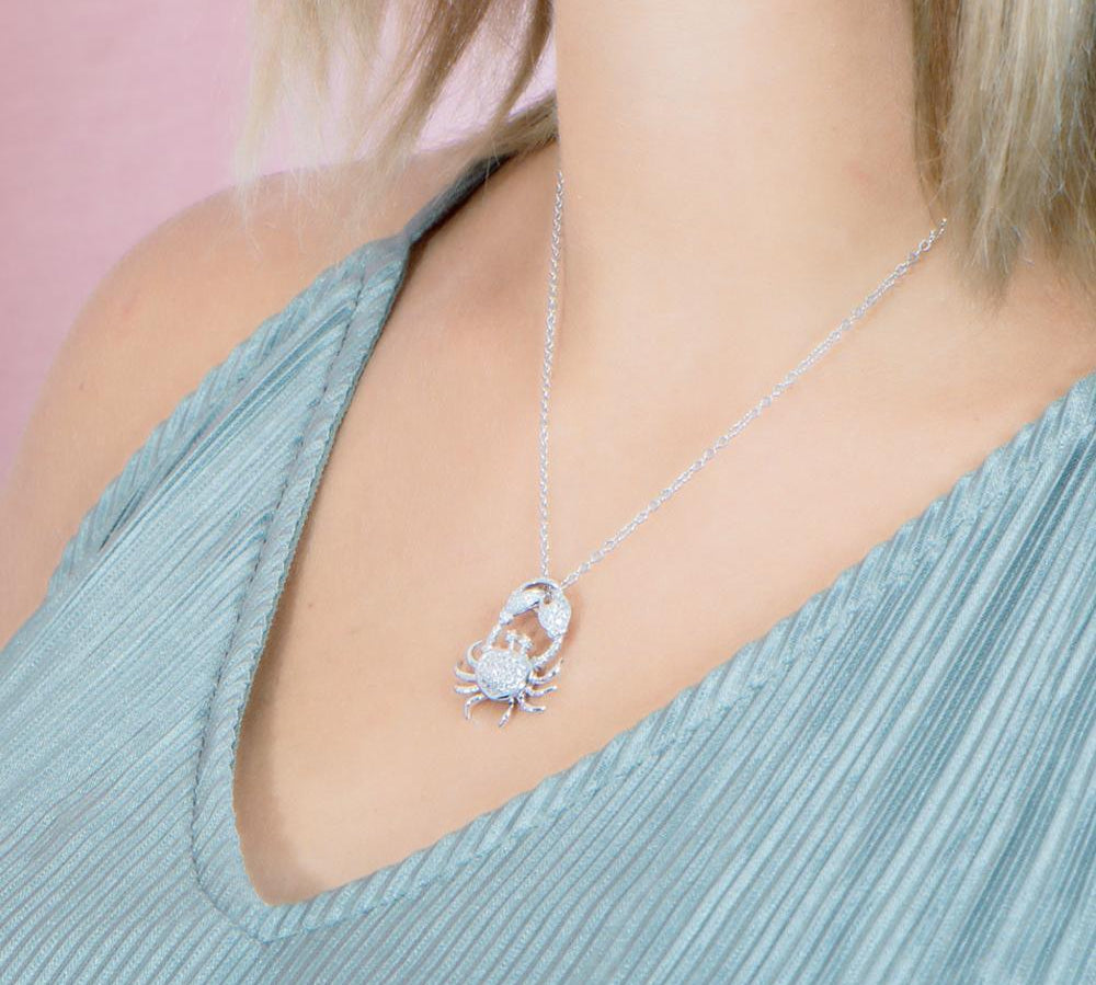 The picture shows a model weaing a 925 sterling silver, white gold plated, pavé crab pendant with topaz.