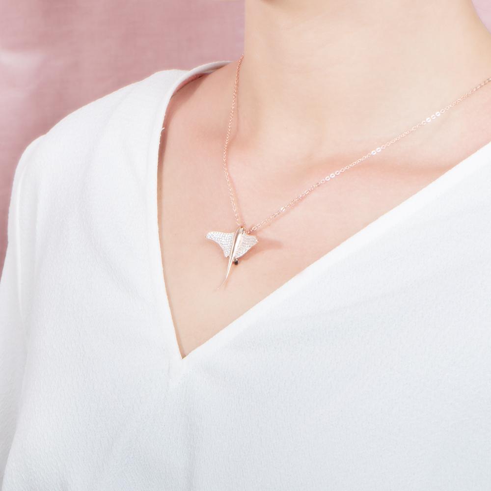 The picture shows a model wearing a 925 sterling silver, rose gold plated, pavé eagle ray pendant with cubic zirconia.