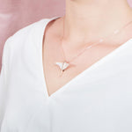 The picture shows a model wearing a 925 sterling silver, rose gold plated, pavé eagle ray pendant with cubic zirconia.