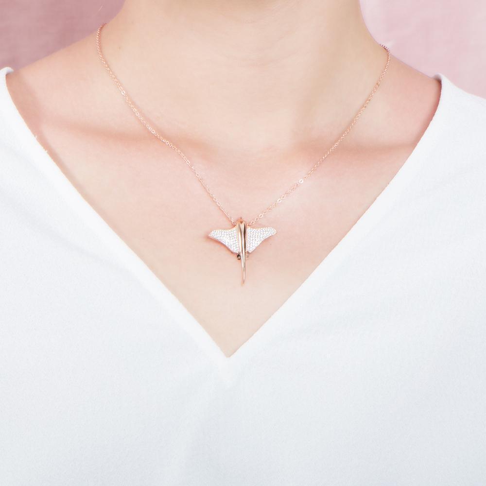 The picture shows a model wearing a 925 sterling silver, rose gold plated, pavé eagle ray pendant with cubic zirconia.