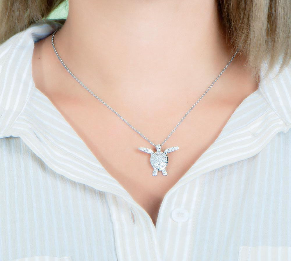 In this photo there is a model with blonde hair and a tan and white striped shirt, wearing a white gold sea turtle pendant with cubic zirconia.