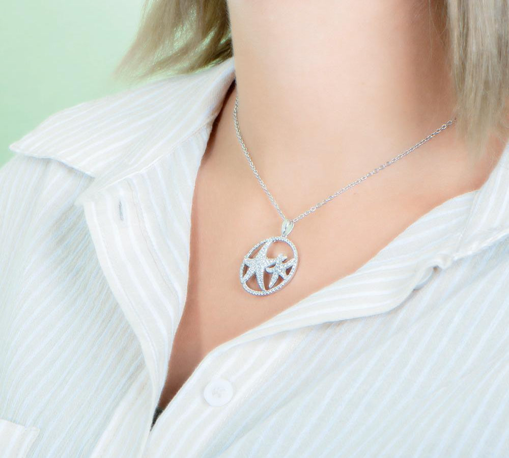 The picture shows a model wearing a 925 sterling silver, white gold vermeil, double starfish circle pendant with topaz.