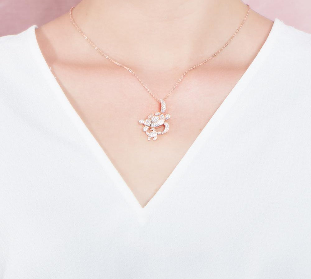 The picture shows a model wearing a 925 sterling silver, rose gold vermeil, double sea turtle pendant with topaz.