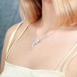 The picture shows a model wearing a 925 sterling silver, white gold-vermeil, dolphin pendant with topaz.