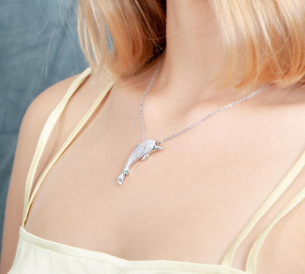 The picture shows a model wearing a 925 sterling silver, white gold-vermeil, dolphin pendant with topaz.