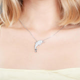 The picture shows a model wearing a 925 sterling silver, white gold-vermeil, dolphin pendant with topaz.