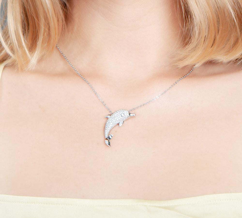 The picture shows a model wearing a 925 sterling silver, white gold-vermeil, dolphin pendant with topaz.