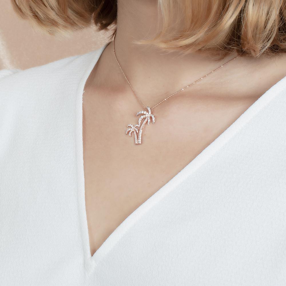 In this photo there is a model turned slightly to the left with blonde hair and a white shirt, wearing a rose gold double palm tree pendant with topaz gemstones.