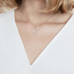 In this photo there is a model with blonde hair and a white shirt, wearing a rose gold double palm tree pendant with topaz gemstones.