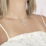 In this photo there is a model turned slightly to the right with blonde hair and a white shirt with purple flowers, wearing a white gold double palm tree pendant with topaz gemstones.