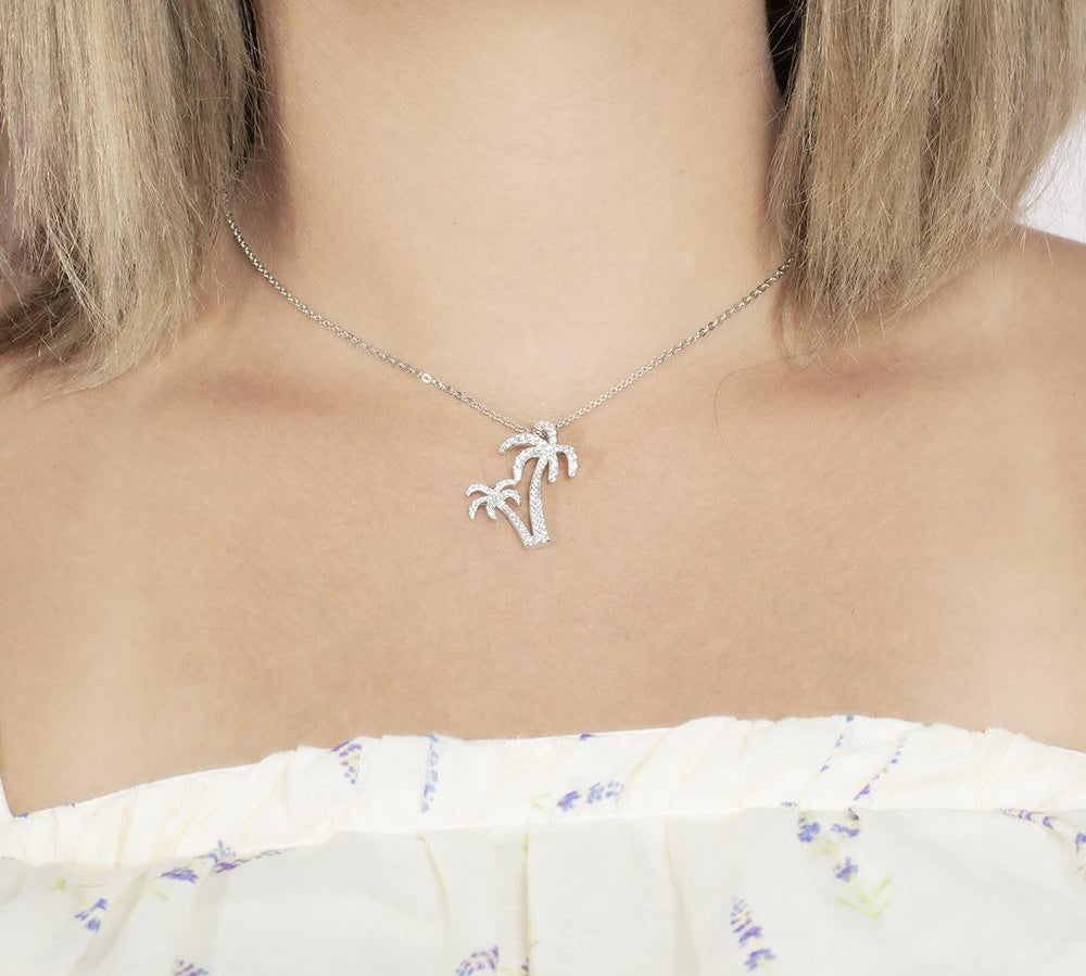 In this photo there is a model with blonde hair and a white shirt with purple flowers, wearing a white gold double palm tree pendant with topaz gemstones.