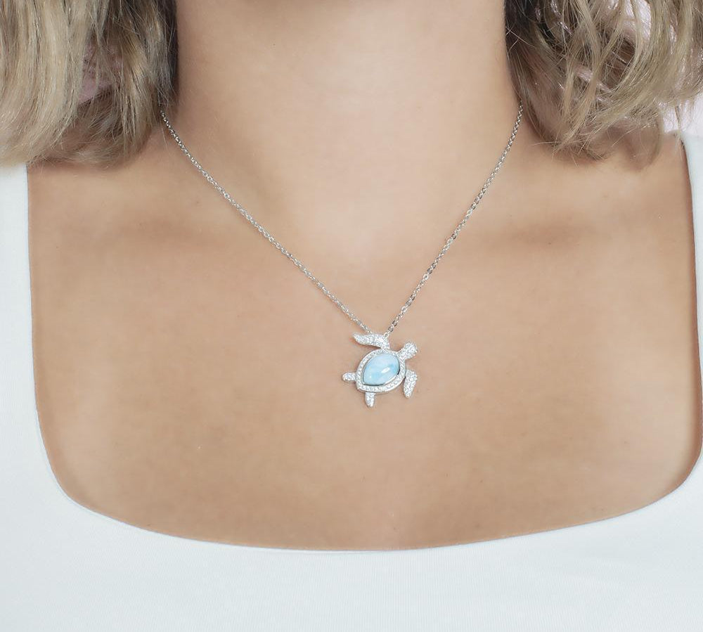 The picture shows a model wearing a 925 sterling silver pavé larimar sea turtle pendant with cubic zirconia.