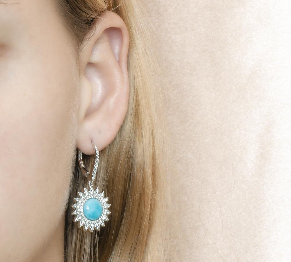 In this photo is a model with blonde hair wearing sterling silver sunflower dangle earrings with blue larimar and topaz gemstones.