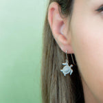 The picture shows a model wearing a 925 sterling silver white gold-vermeil sea turtle hook earring with topaz.