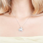 The picture shows a model wearing a 925 sterling silver, white gold plated, sea turtle pendant with topaz.