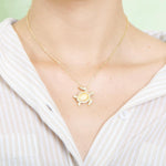 The picture shows a model wearing a 925 sterling silver, yellow gold plated, sea turtle pendant with topaz.