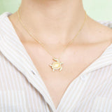 The picture shows a model wearing a 925 sterling silver, yellow gold plated, sea turtle pendant with topaz.