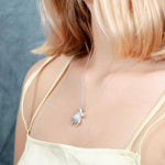 The picture shows a model wearing a 925 sterling silver, white gold plated, sea turtle pendant with topaz.