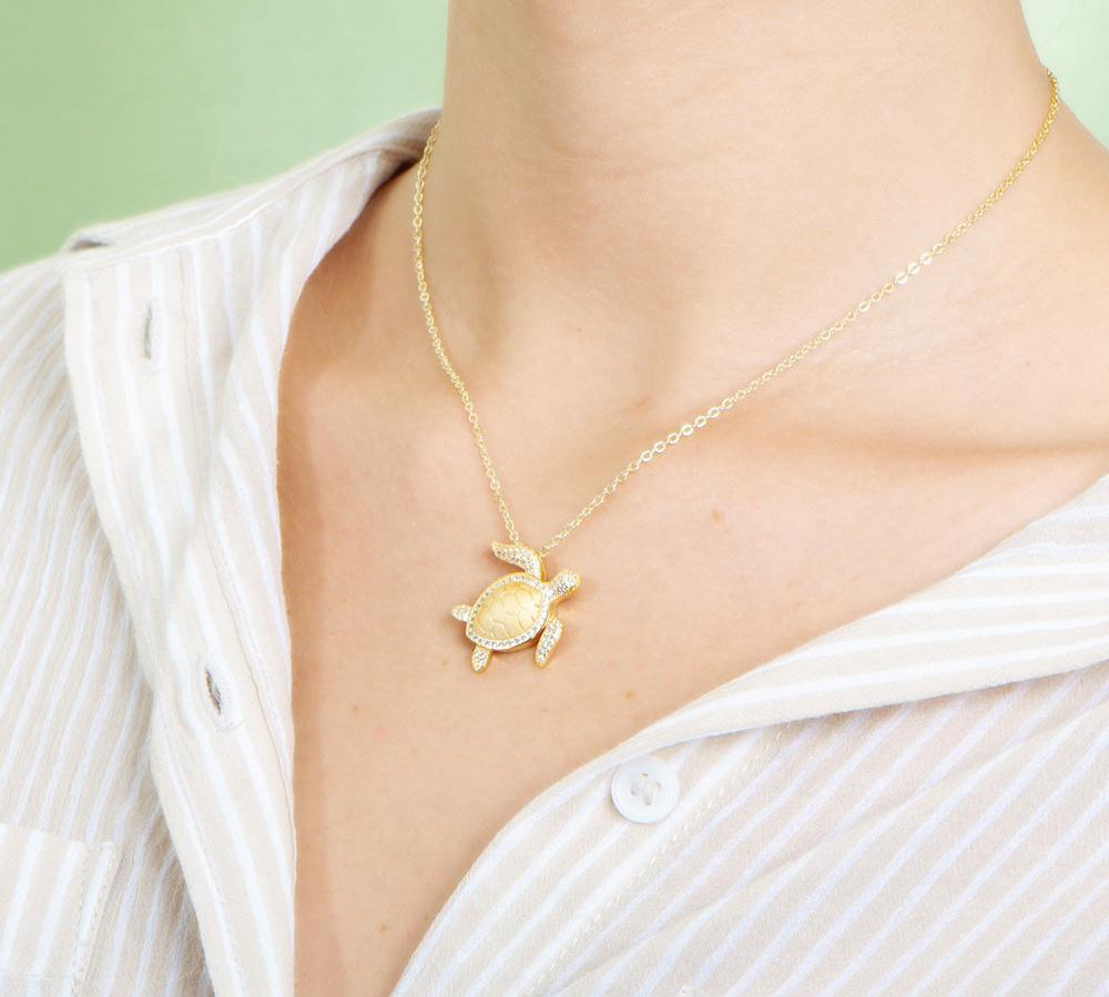 The picture shows a model wearing a 925 sterling silver, yellow gold plated, sea turtle pendant with topaz.